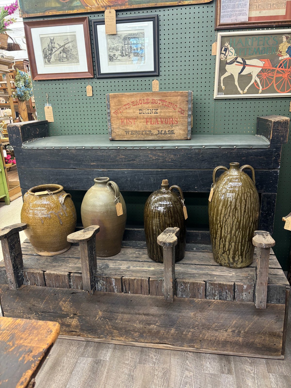 Antique ceramic jars and jugs displayed on wooden stands in front of a dark wooden beam in a vintage shop