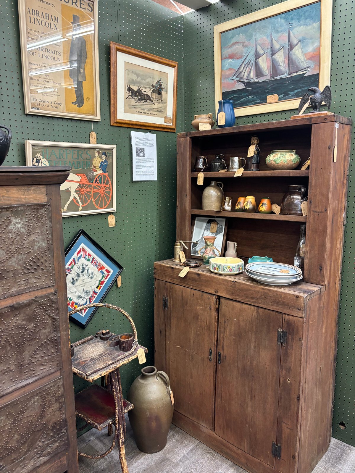 Antique wooden cabinet and furniture display on green pegboard wall with nautical decor and vintage items