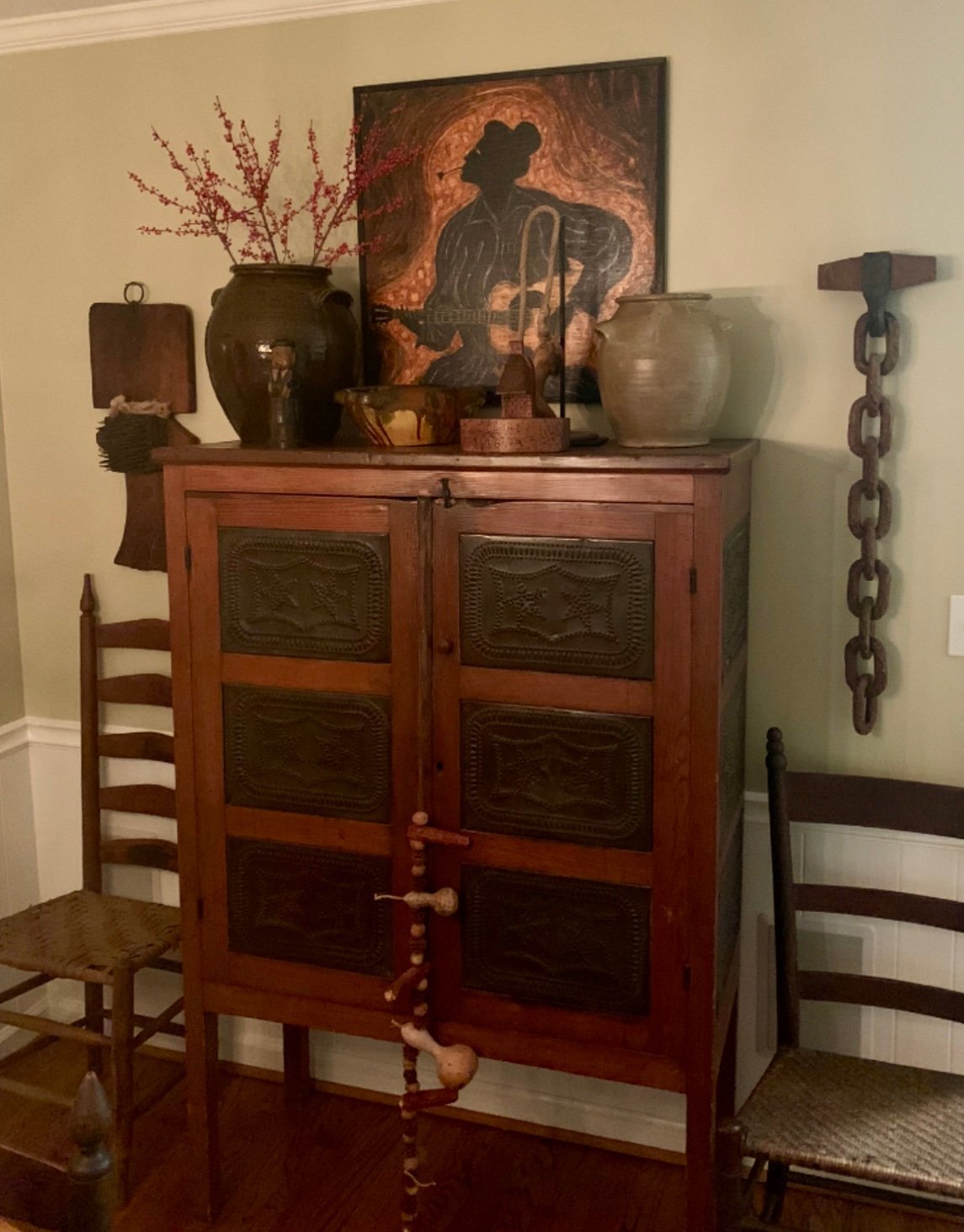 Wooden cabinet with glass doors decorated with pottery, framed artwork, and decorative items on top